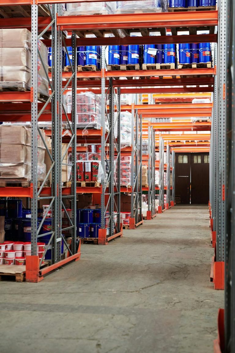 A warehouse aisle with tall metal shelves filled with boxed and wrapped goods showcases an impressive array of protection products. The shelves are organised, the concrete floor is visible, and bright lighting highlights the orderly rows of products.